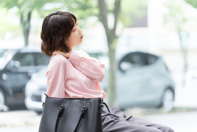 片方でバッグを持ち肩こりに悩む女性